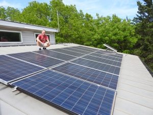 Image of man kneeling next to solar panels on the roof of a home